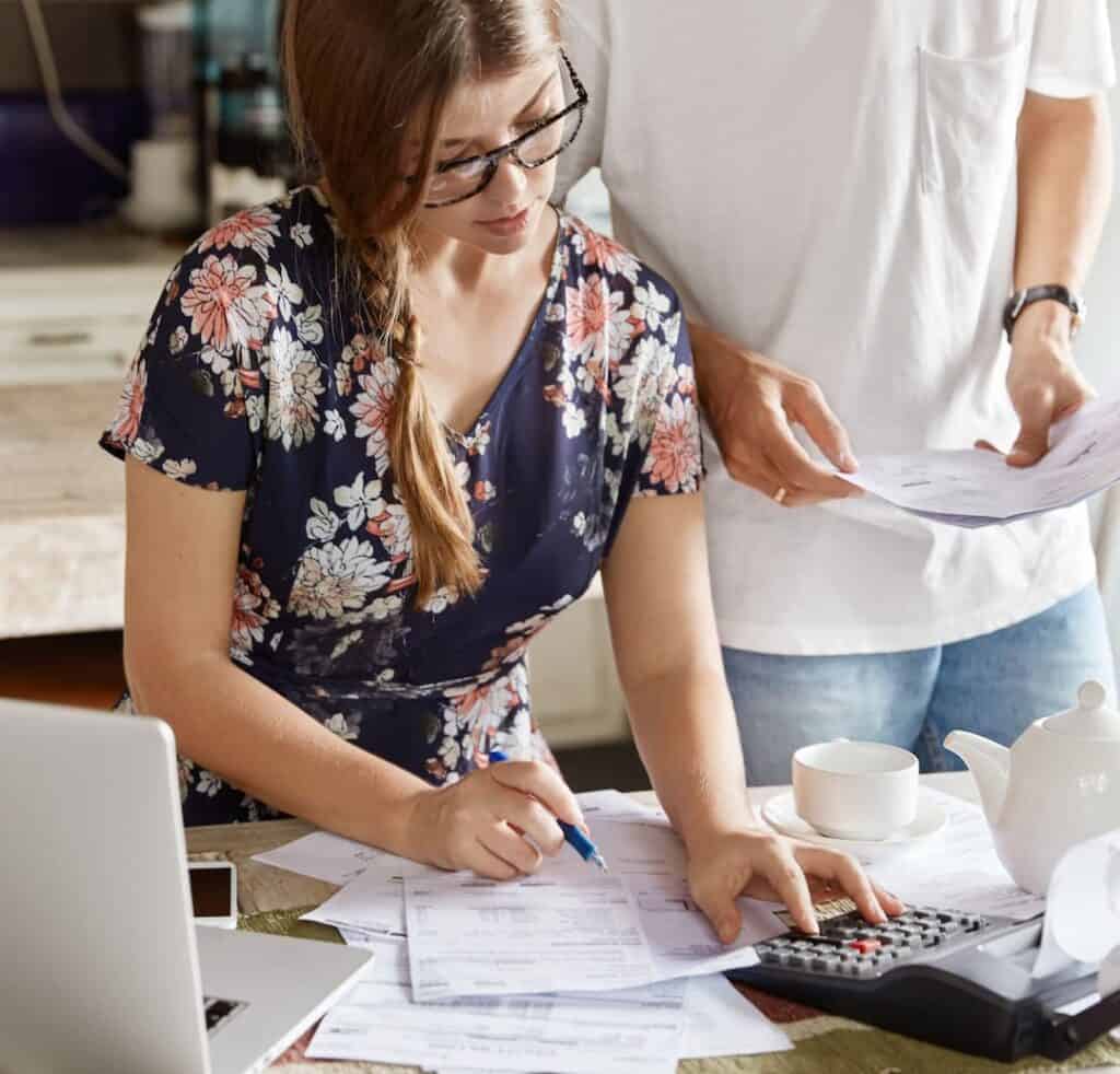 Mujer y hombre mirando su presupuesto familiar en un escritorio junto a un computador